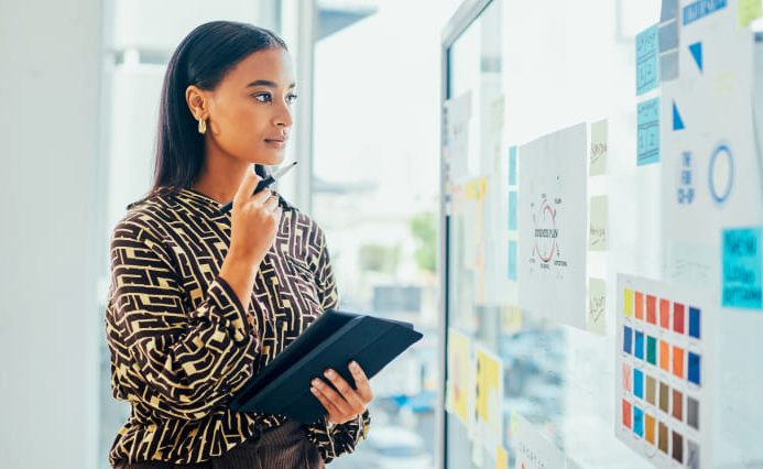 A woman is looking at a white board,filled with stats and colorful papers in deep thought.