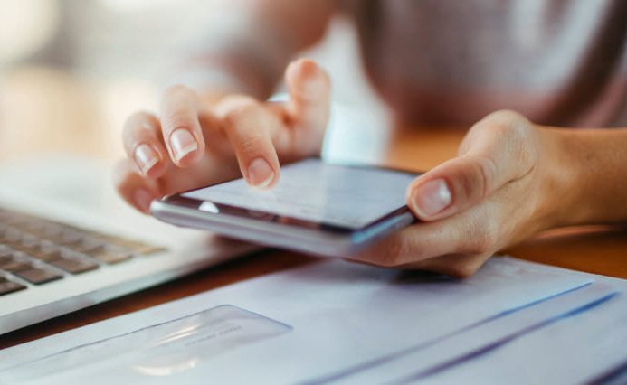 A person is holding their smartphone over a desk cluttered with papers.