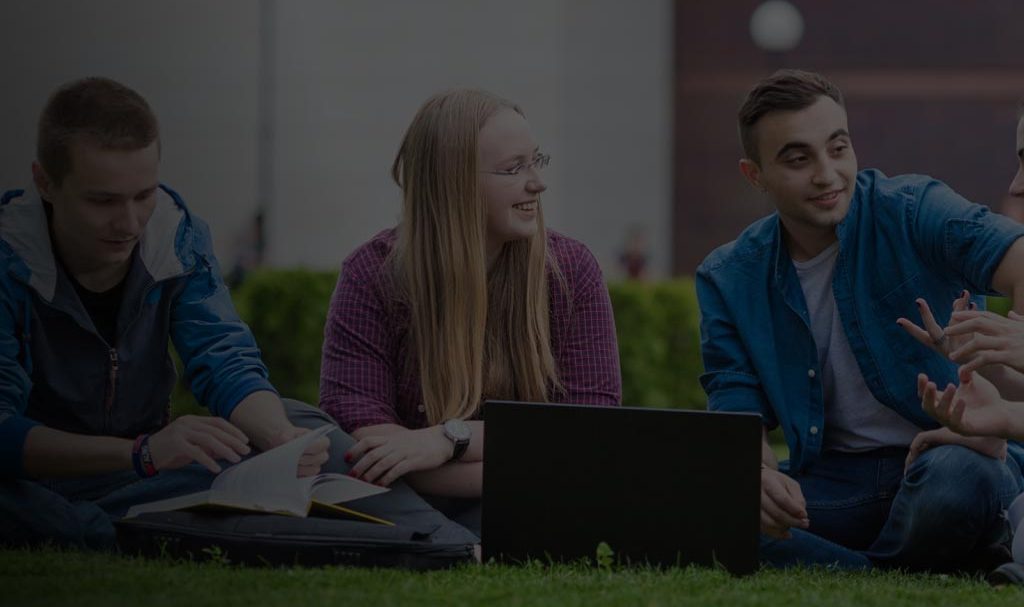 students sitting on a lawn with a laptop and talking