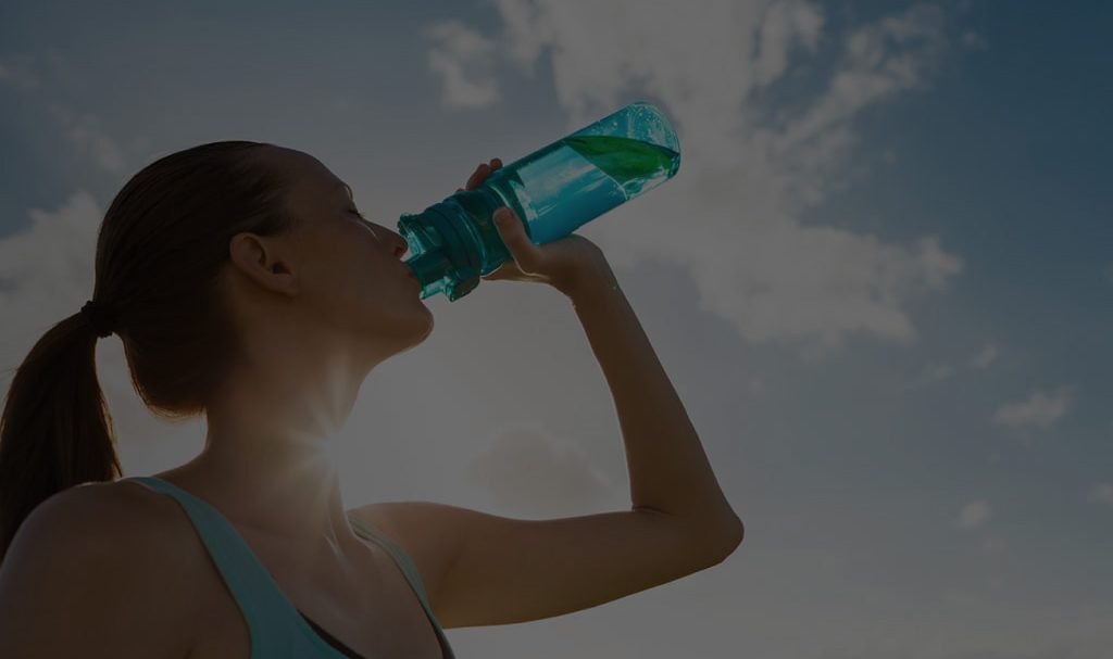 woman drinking water from a bottle with the sun and sky in the background