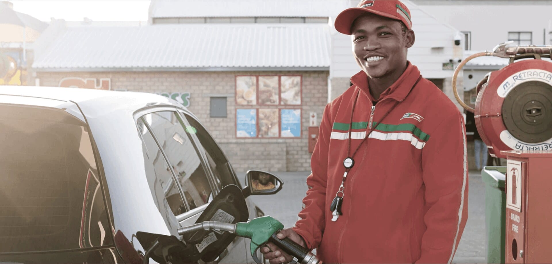Smiling gas station attendant in a red uniform pumping fuel into a car
