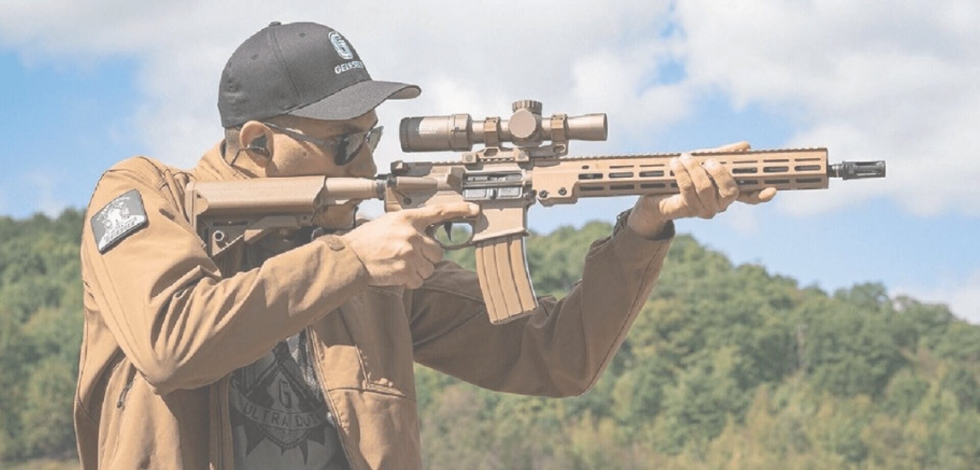 Person aiming a scoped rifle at an outdoor shooting range while wearing protective eyewear and hearing protection, demonstrating precision marksmanship.