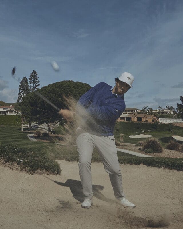 Links Golf 66 Golfer hitting a bunker shot during a round of golf, sending sand into the air while navigating a challenging course hazard.