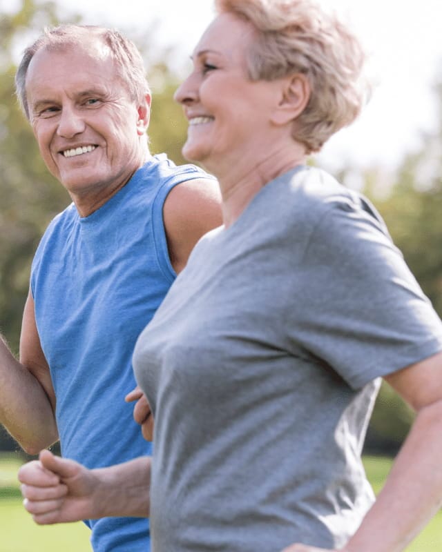 Older man and woman jogging outdoors in a park on a sunny day