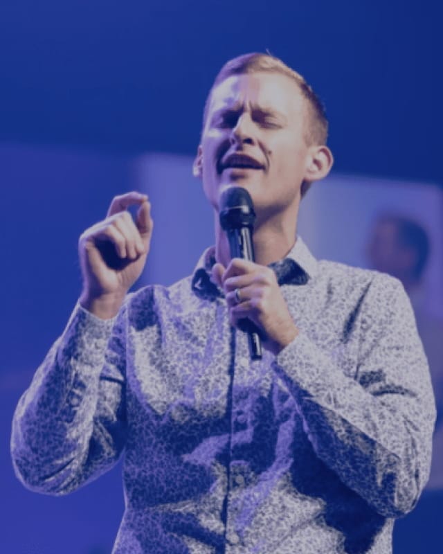Retail Summits 56 Speaker presenting on stage with a microphone, engaging an audience during a live conference, summit, or professional event.