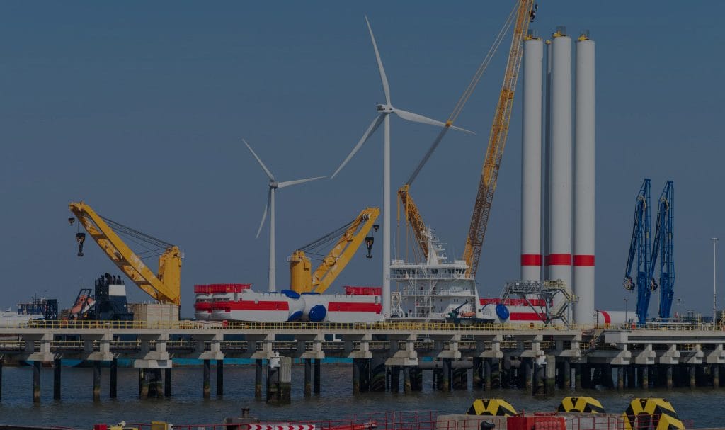 Windmills and heavy machinery are placed on a coastline and jetty