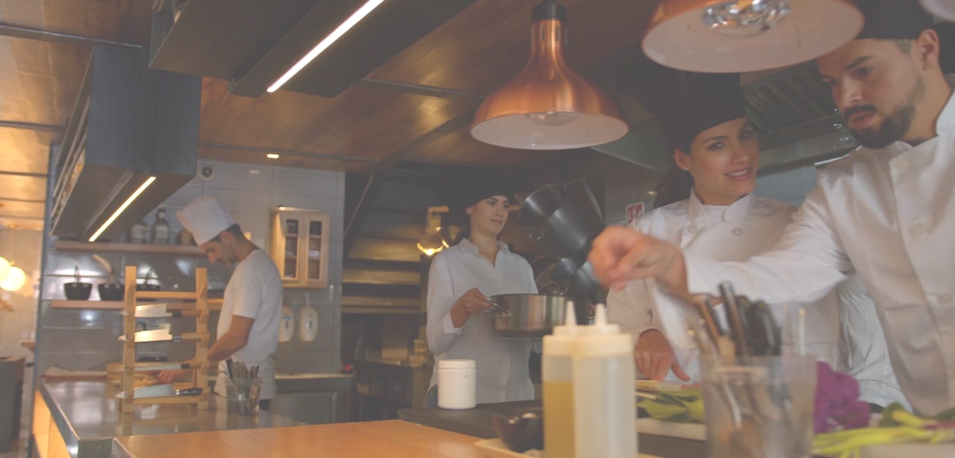 Chefs working together in a commercial kitchen, preparing food under hanging copper lights