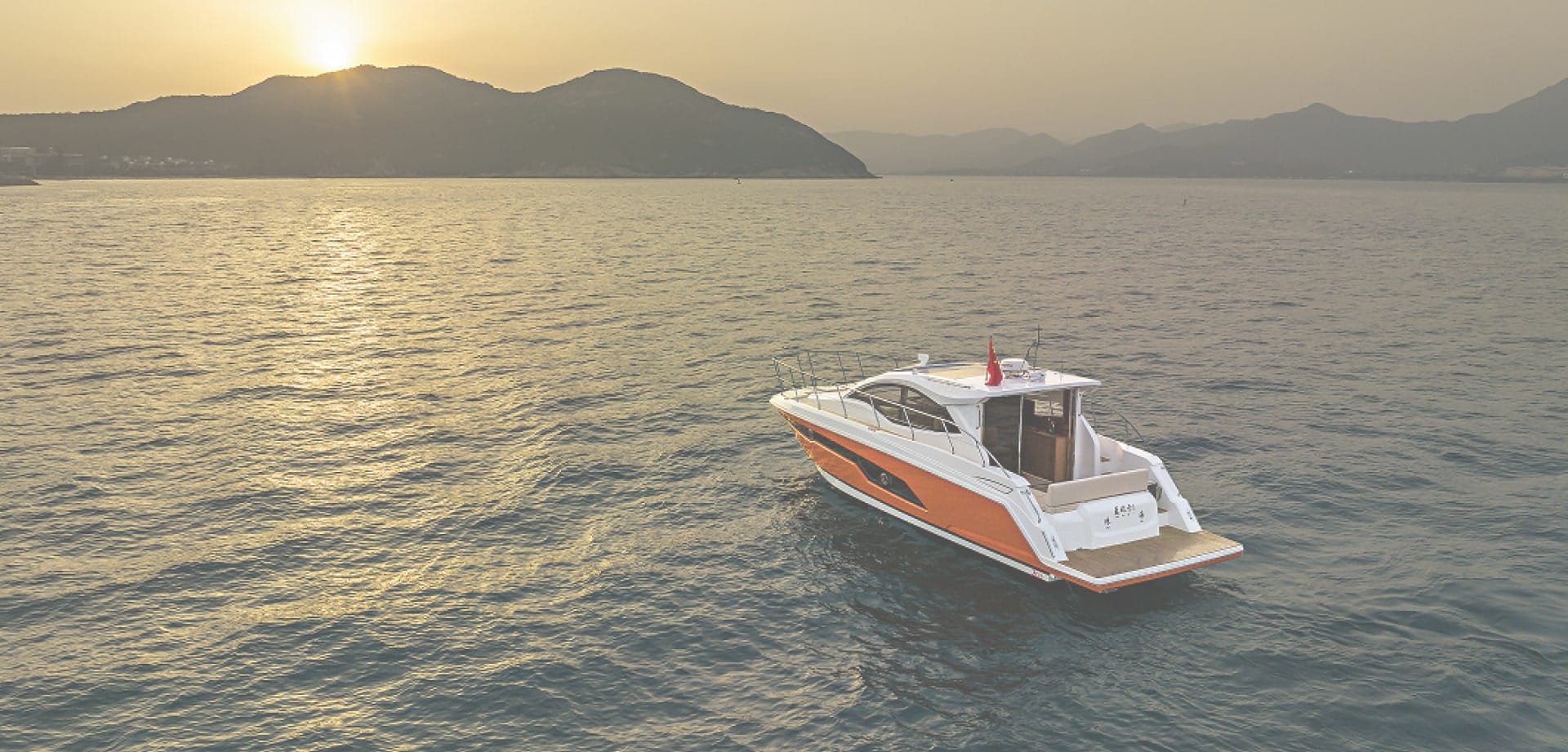 Motor yacht cruising on calm water at sunset with mountains in the distance