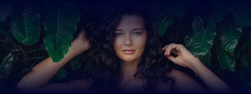 Portrait of a woman with curly hair framed by large green leaves, looking at the camera