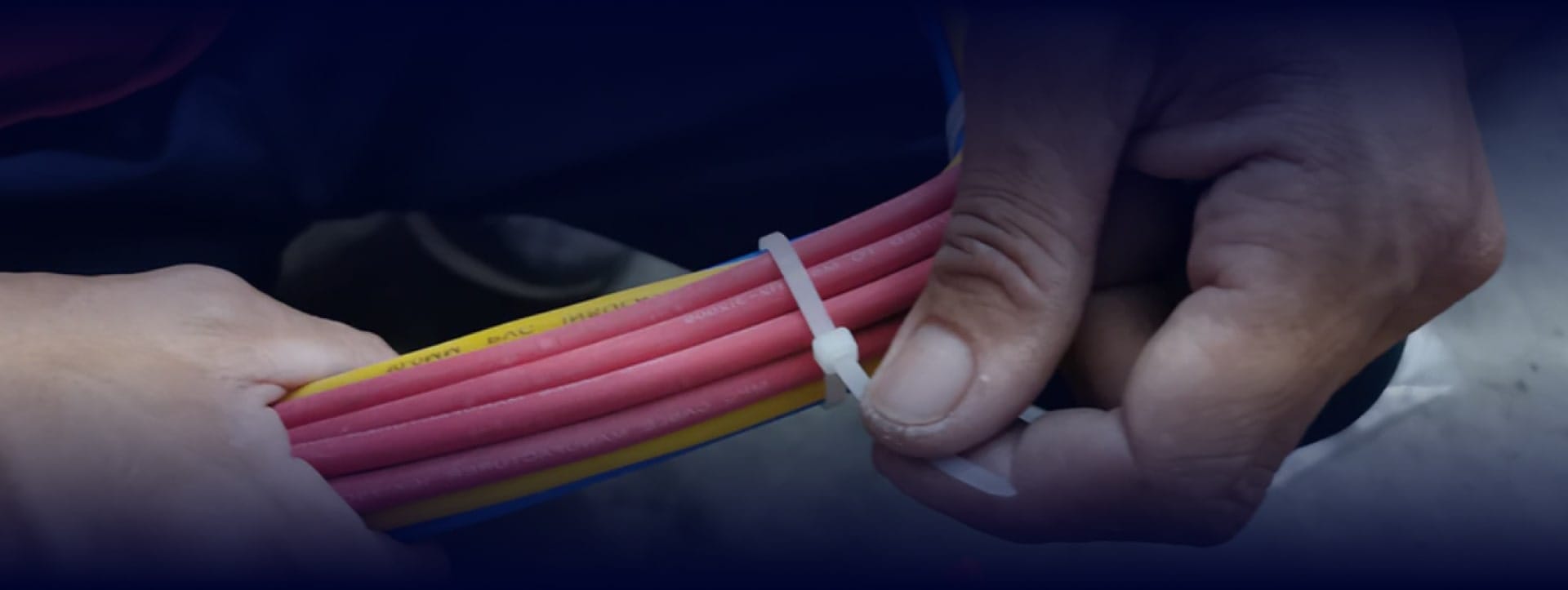 Close-up of hands tightening a zip tie around bundled wires