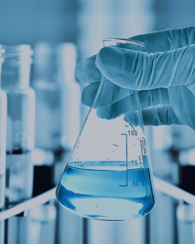 Background image for H2 Compiance's case study showing a gloved hand holding a laboratory flask with blue liquid