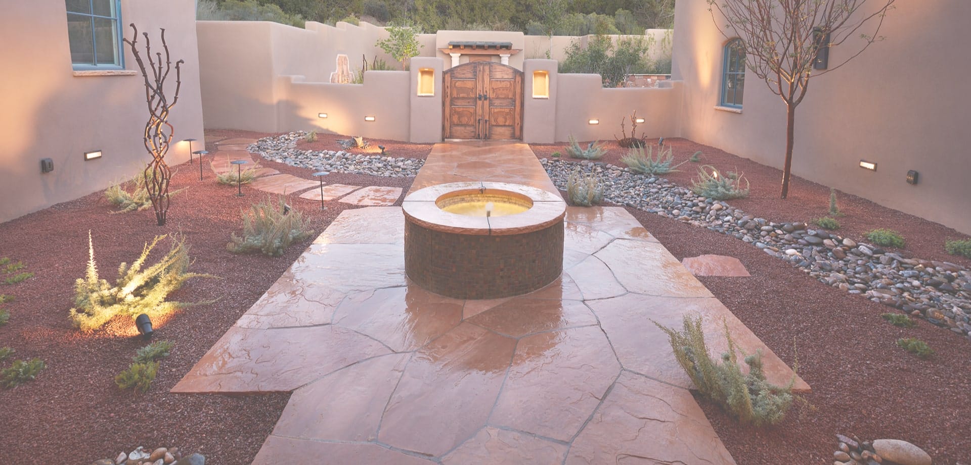 Background image for Urbanna's case study showing a courtyard with stone walkway, water feature and desert landscaping at dusk