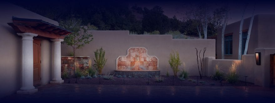 Background image for Urbanna's case study showing a home courtyard with tiled wall fountain and landscape lighting at night