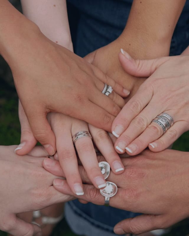 arnold_jewelers_background_4 Close-up of several hands placed together, each wearing different silver and diamond rings and bands.