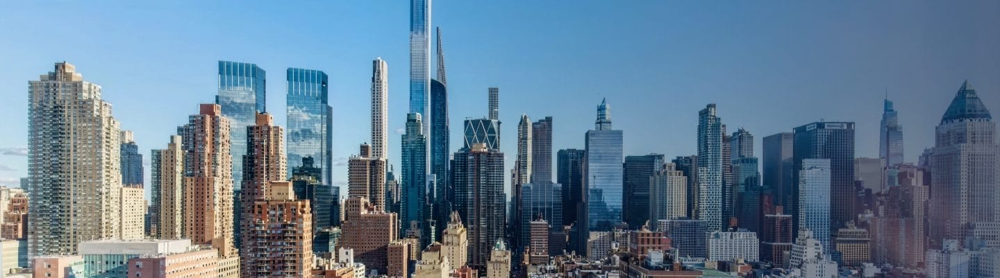 City skyline with a dense cluster of high-rise buildings and glass towers under a clear blue sky.