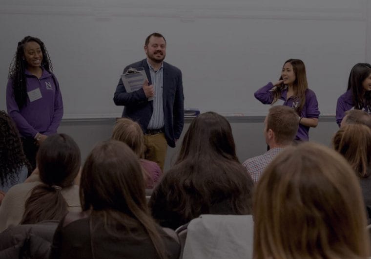 education-website-design-northwestern-background Audience seated in a classroom while a speaker and student ambassadors stand at the front during a Northwestern University event.