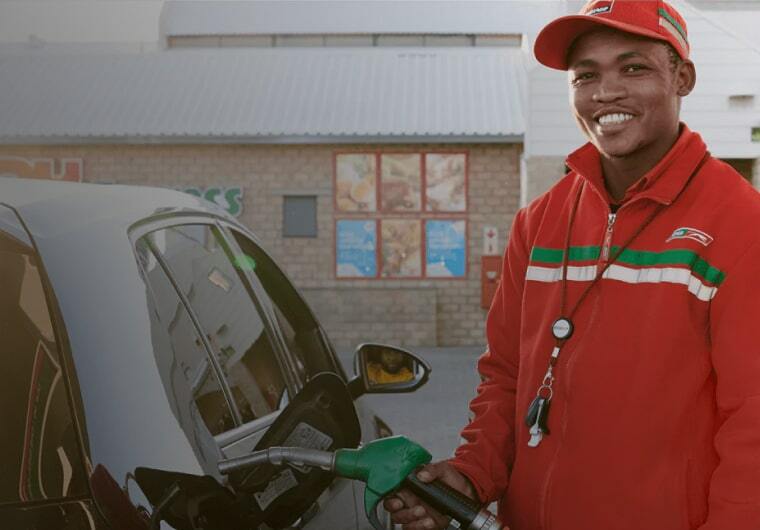 Fuel station attendant in red uniform refueling a black car at a gas station forecourt