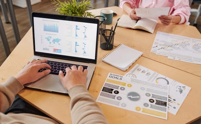 SEO analyst reviewing website performance data and reporting metrics on a laptop during a planning meeting
