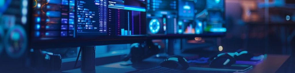 Multiple monitors displaying code, data charts and analytics dashboards in a blue-lit development workspace.