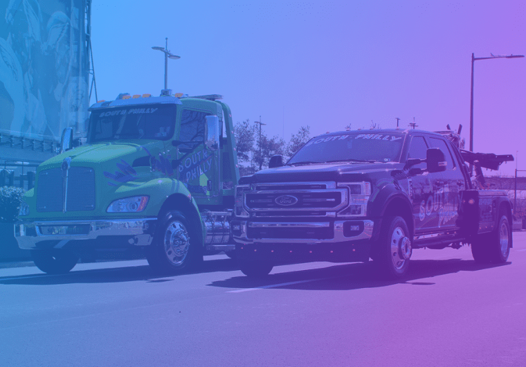 Two South Philly towing trucks driving side by side on a city street