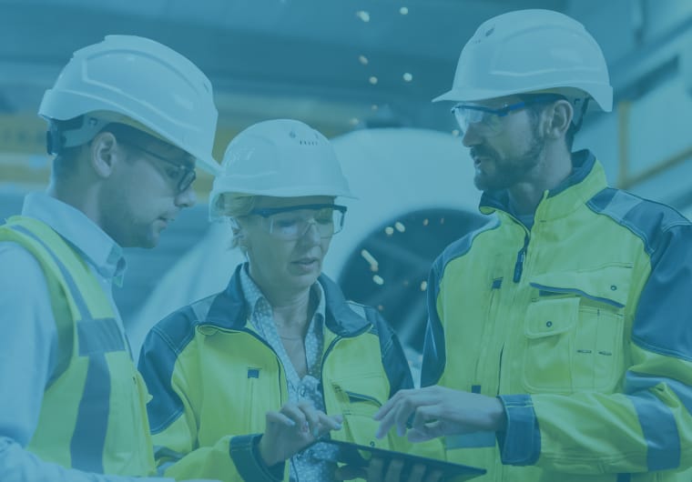 Three construction professionals wearing white hard hats, safety glasses, and high-visibility jackets