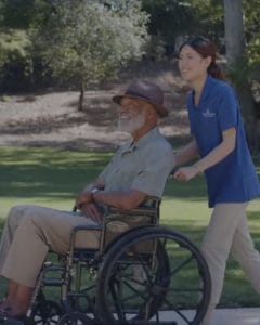 Branding Agency In Chicago 116 Caregiver pushing an elderly man in a wheelchair along a paved path in a sunny park.