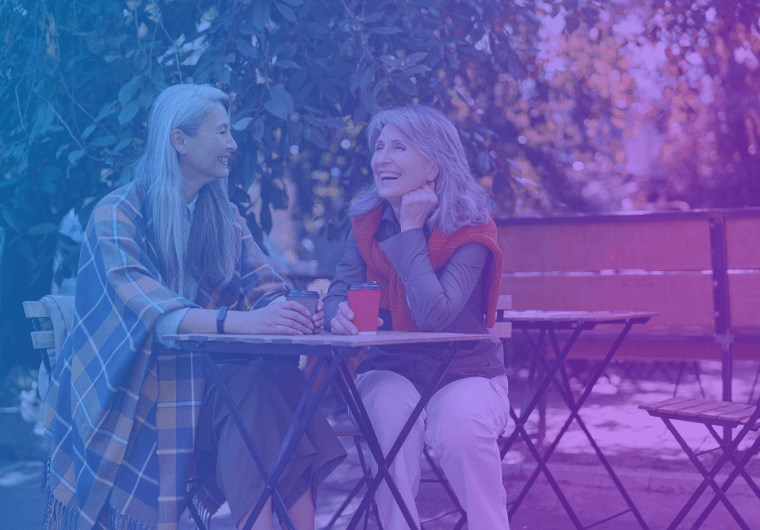 Two women sitting at an outdoor café table, smiling and talking