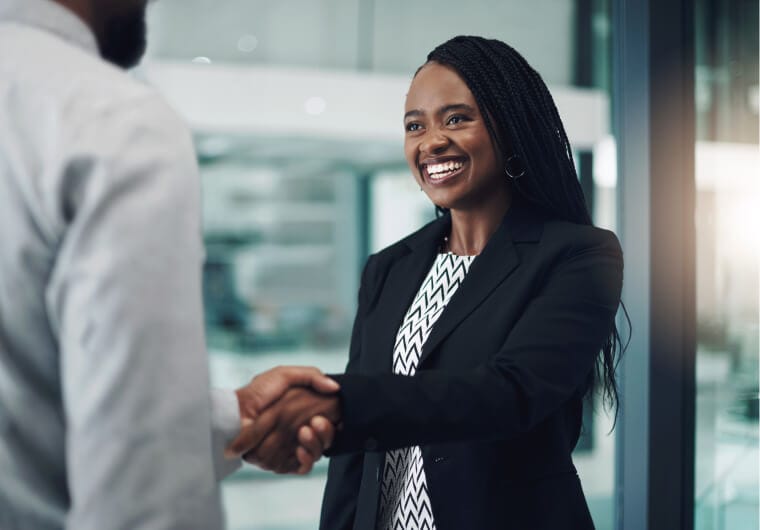 Smiling businesswoman in a blazer shaking hands with a colleague in a modern office
