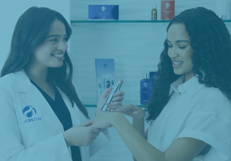 A clinician in a white coat smiles while applying or demonstrating a product on a client’s hand