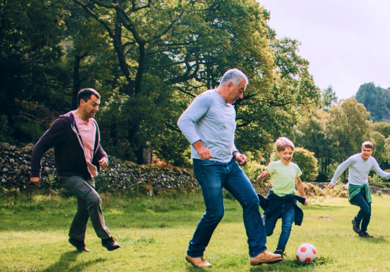Four people of different ages playing soccer together on a grassy field in a park