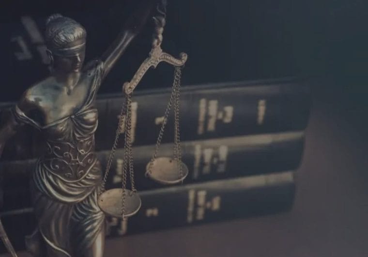 Bronze Lady Justice statue holding scales in front of stacked law books