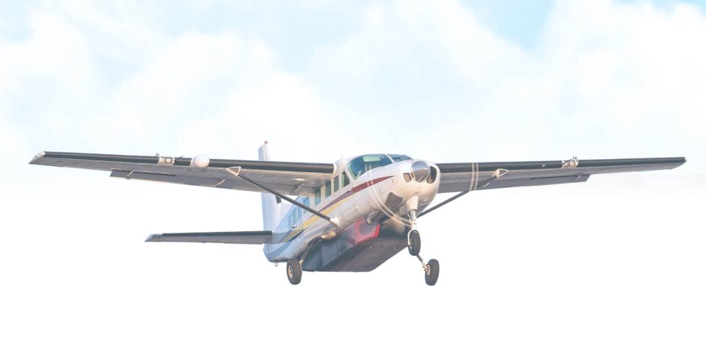 White twin-engine turboprop aircraft approaching for landing against a bright overcast sky