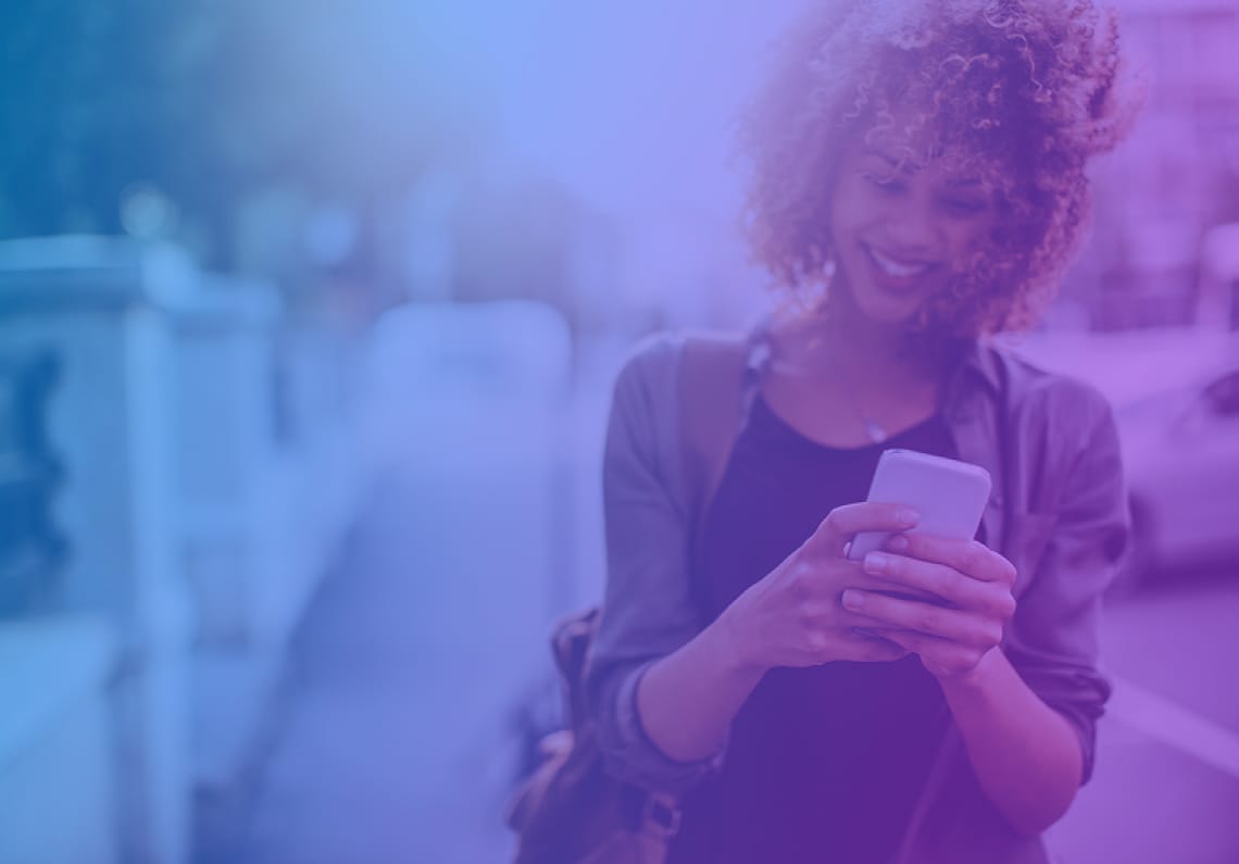 Woman with curly hair smiling while using a smartphone outdoors, with a teal blue color overlay