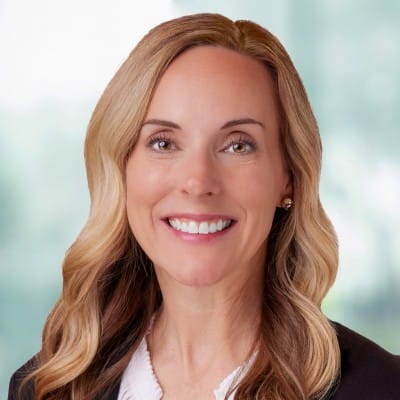 Brand Identity 82 Smiling woman with wavy blonde hair wearing a dark blazer over a white top, photographed against a softly blurred light background