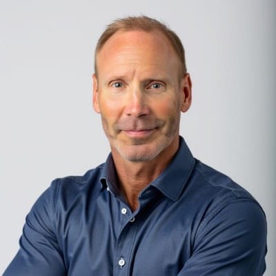 Franchise Marketing Agency 42 Man with short light-brown hair wearing a blue button-up shirt, posing with arms crossed against a plain light gray background