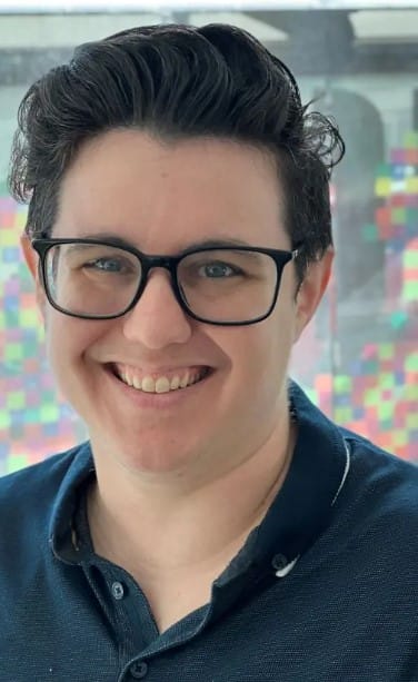 Franchise Marketing Agency 68 Smiling person with dark hair and black glasses wearing a navy collared shirt, with a colorful blurred background behind them