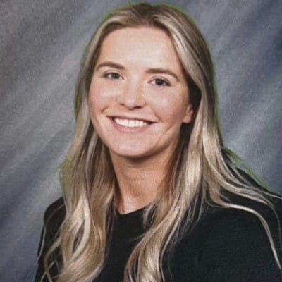 Web Design 86 Smiling woman with long blonde hair wearing a black top, photographed against a gray studio-style background