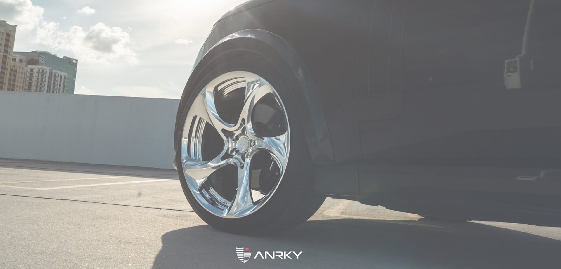 Close-up of a black vehicle fitted with a polished five-spoke ANRKY wheel, photographed on a sunlit rooftop with the ANRKY logo below